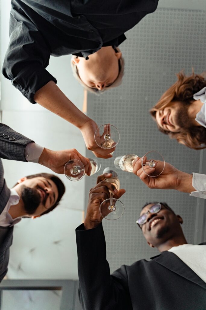 A diverse group of adults clinking champagne glasses in celebration, viewed from below.