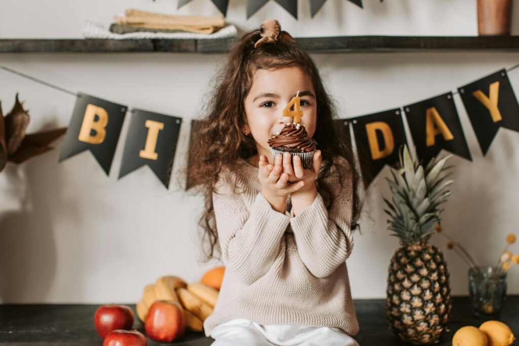A joyful child celebrates her fourth birthday with a chocolate cupcake indoors.